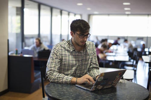 Graduate student working off laptop in lounge area