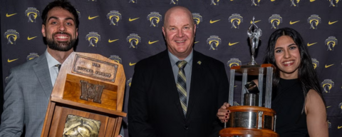 Two athletes donned in formal wear posing with their huge trophies 