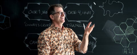 Craig S. Kaplan juggles chalk in front of a blackboard with illustrations from his research