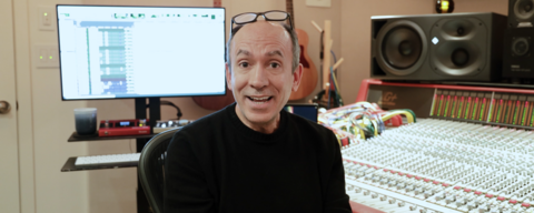 A Portuguese man wearing a long-sleeve black shirt and glasses on his forehead posing in front of a music soundboard/keyboard