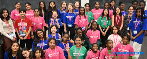 A group of girls donning blue, red and green t-shirts and nametags standing in front of a blackboard