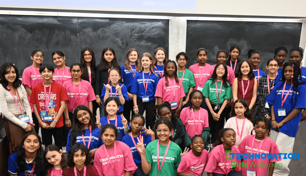 A group of girls donning blue, red and green t-shirts and nametags standing in front of a blackboard
