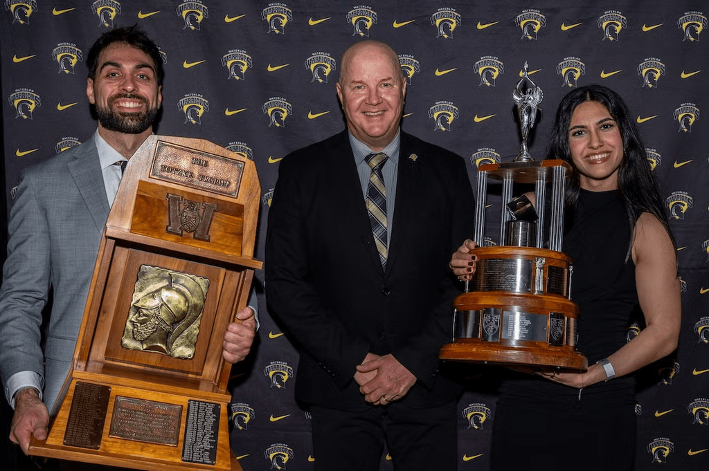 Two athletes donned in formal wear posing with their huge trophies 