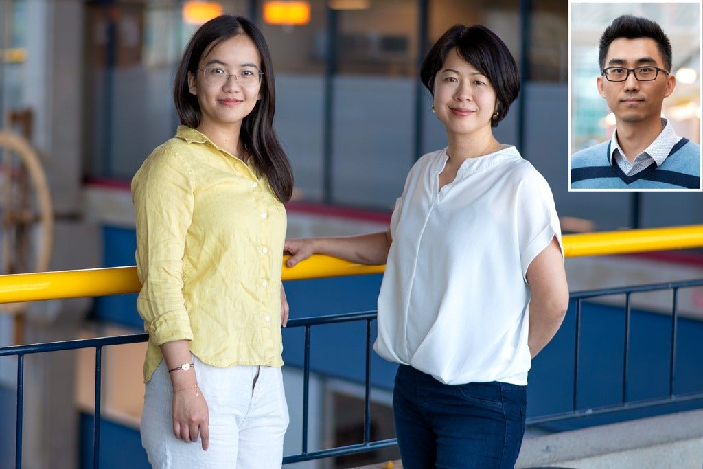 Two women stand together near a yellow railing in a modern indoor space. A smaller image of a man is inset in the corner.