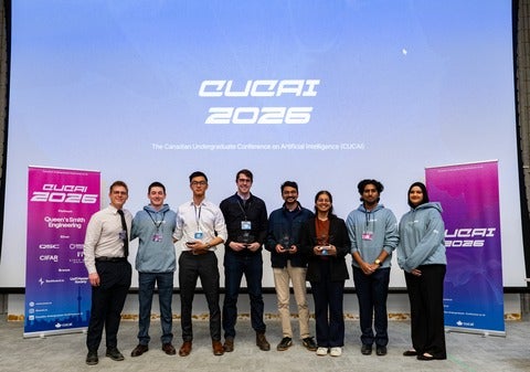 A group of people wearing event lanyards and holding a small trophy posing in front of an ocean-blue-screen, with the words "CUCAI 2026" 