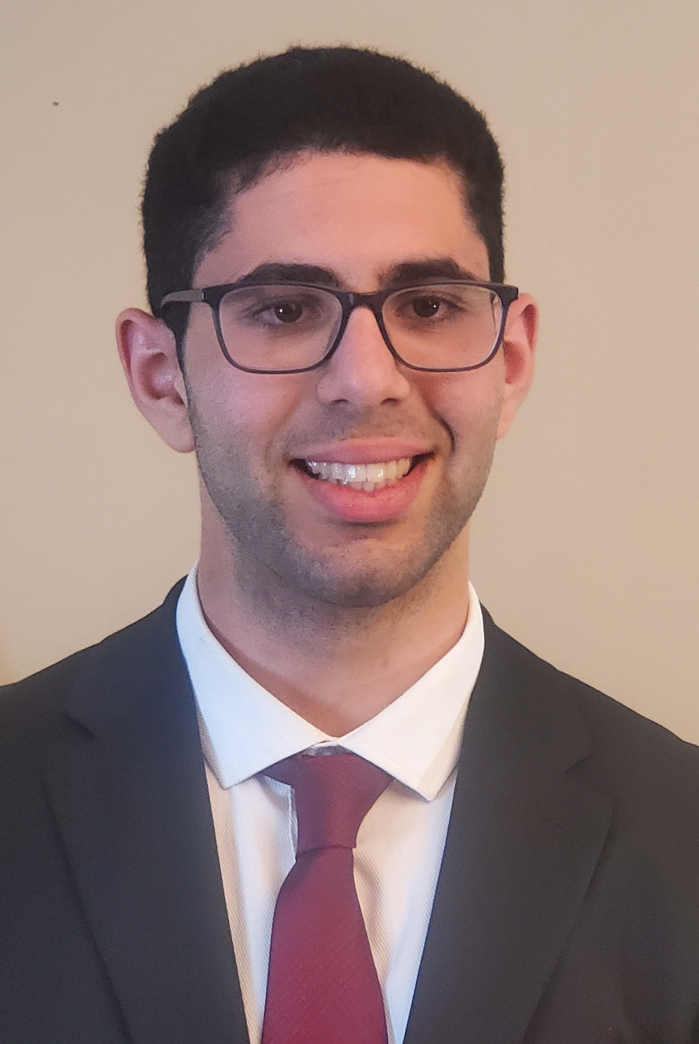 A man wearing a suit and maroon tie and glasses