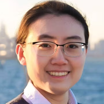 An Asian woman wearing glasses in front of a body of water