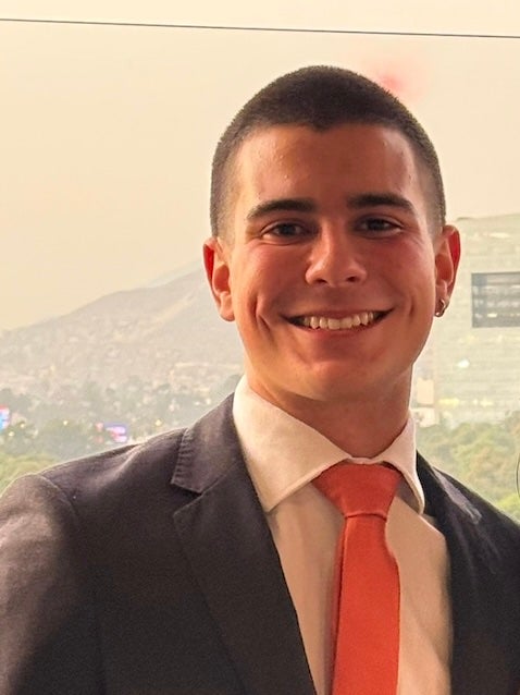 A young man with a buzzcut donning a pink tie and grey suit 