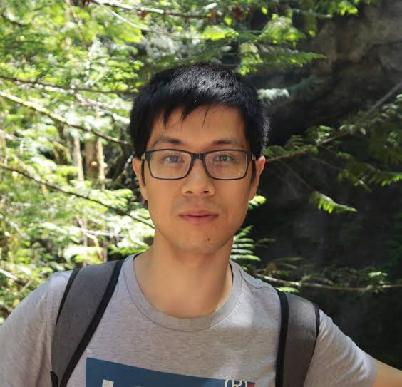 Photo of an Asian Man in a forest. He is wearing a grey t-shirt and a backpack