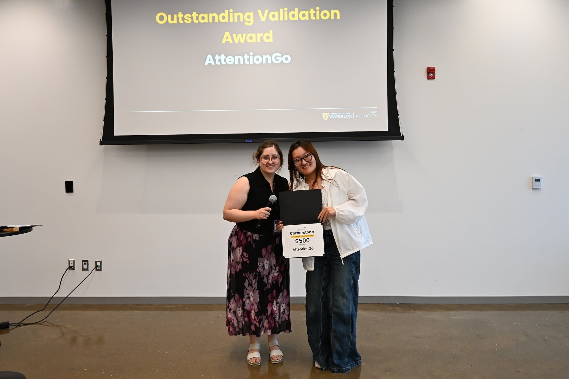 Bella smiling and holding her award "Cornerstone's Outstanding Validation Award $500". She is holding it with her Velocity mentor, Krysta Traianovski